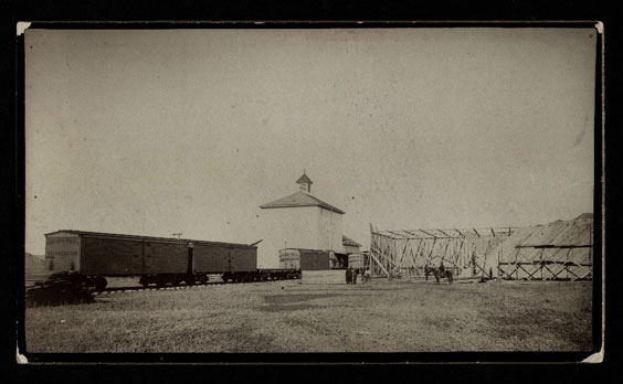 A white building sits behind train tracks with a few train cars on it