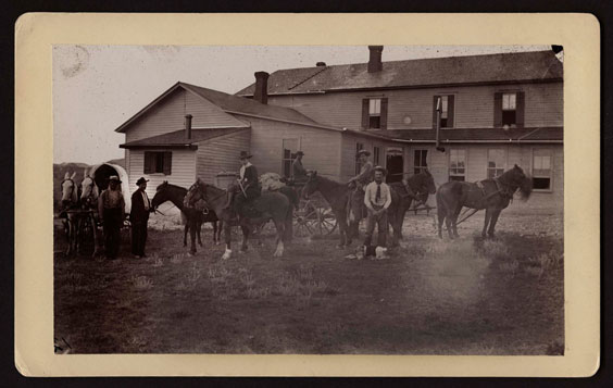 Men and horses stand in front of an old house