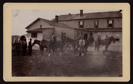 Men and horses stand in front of an old house